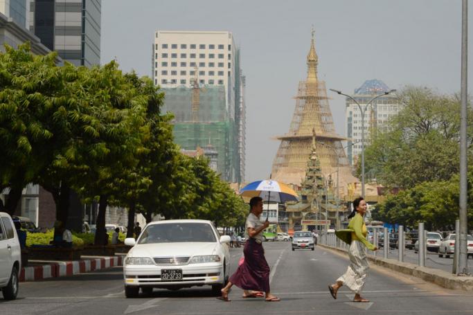 Pedestrians cross the street across Sule pagoda, seen in the background, in central Yangon. Photo: AFP
