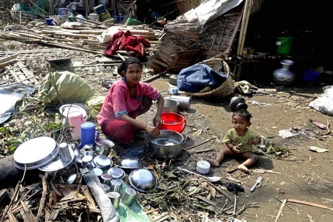 A Rohingya woman washes dishes near her damaged house at the Thae Chaung Muslim internally displaced people (IDPs) camp near Sittwe, Rakhine State, Myanmar, 17 May 2023.  Photo: EPA