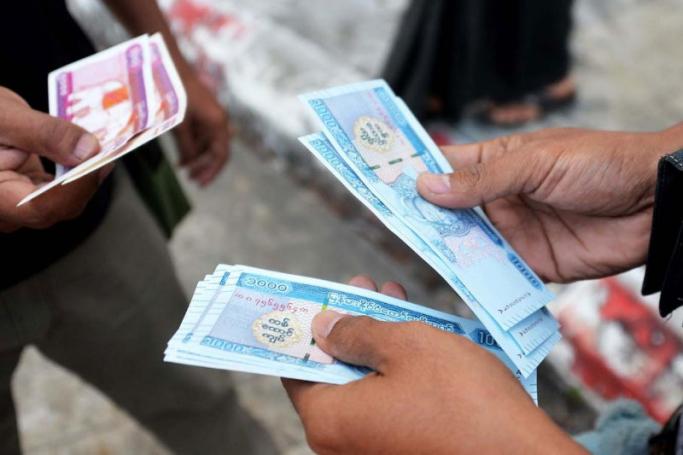 People hold new kyat banknotes featuring a portrait of the late general Aung San, outside Myanmar Economic Bank in Nay Pyi Taw. Photo: AFP