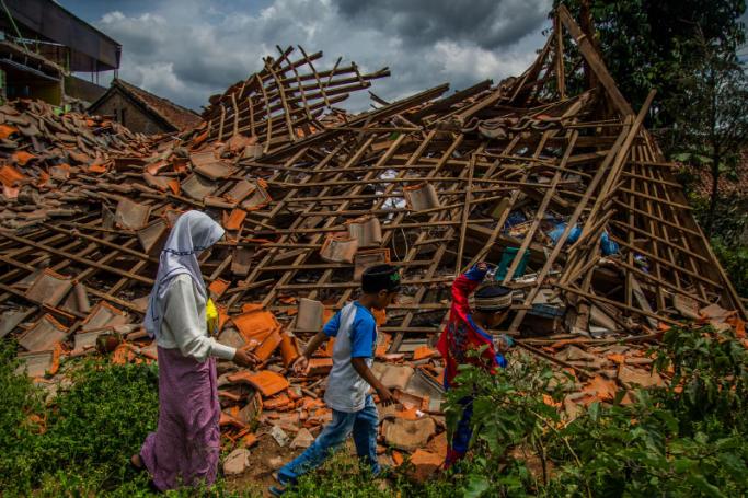 Children of earthquake victims walk past a collapsed house at Cugenang village in Cianjur, West Java on December 1, 2022, ten days after a 5.6-magnitude earthquake left 328 people dead. Photo: AFP