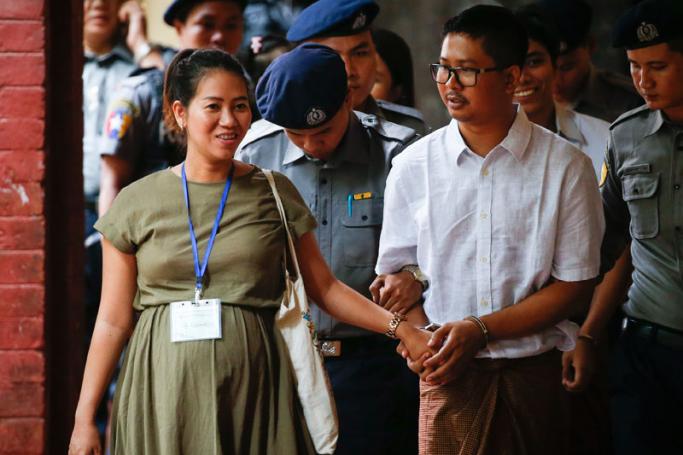 Detained Reuters journalist Wa Lone (R),  escorted by police, holds the hand of his pregnant wife Pan Ei Mon (L)  as he arrives at the court in Yangon, Myanmar, 23 July 2018. Photo: Lynn Bo Bo/EPA