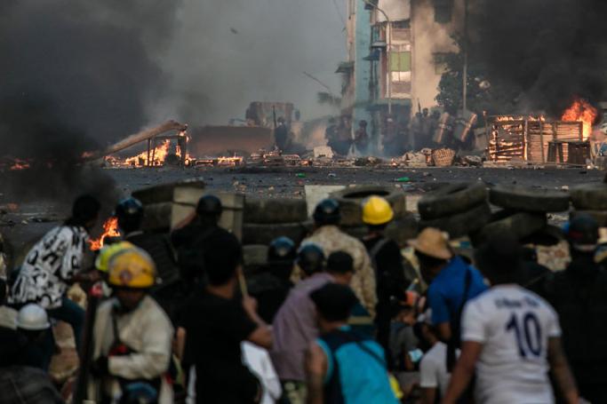 Police officers (background) take position along a road as protesters take cover behind makeshift barricades during a crackdown on demonstrations by protesters against the military coup in Yangon on March 16, 2021. Photo: AFP