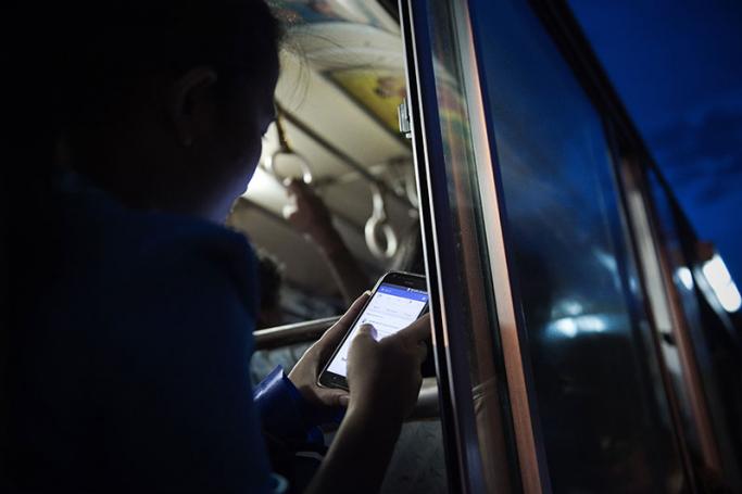 A young woman looks at her Facebook wall while she travels on a bus in Yangon. Photo: AFP
