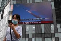A woman uses her mobile phone as she walks in front of a large screen showing a news broadcast about China's military exercises encircling Taiwan, in Beijing on August 4, 2022. Photo: AFP