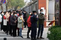 People wait in line to receive Covid-19 coronavirus vaccination booster shots as a security guard checks body temperature of a man along a street in Beijing on October 30, 2021. Jade GAO / AFP