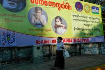 A woman wearing a protective face mask walks past a large poster promoting health and education to curb the spread of the novel coronavirus disease (COVID-19) in the downtown area of Yangon, Myanmar, 02 April 2020. Photo: Lynn Bo Bo/EPA