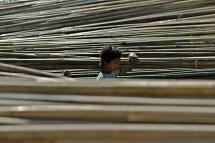 A man loads bamboo poles on his shoulder as he walks passed piles of bamboo poles. Photo: Lynn Bo Bo/EPA
