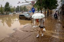 A woman walks on a muddy street next to damaged by flood cars during a downpour in Mentougou District, west of Beijing, China, 01 August 2023. Photo: EPA