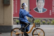 A man in protective gear rides a bicycle on the street past the poster of Chinese president Xi Jinping, amid the ongoing Covid-19 lockdown in Shanghai, China, 23 May 2022. Photo: EPA