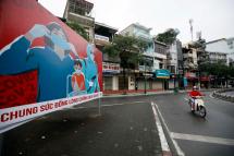 A woman rides motorbike past a billboard about the Covid-19 coronavirus in Hanoi, Vietnam. Photo: EPA