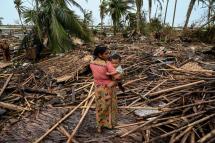 A Rohingya woman carries her baby next to her destroyed house at Basara refugee camp in Sittwe on May 16, 2023, after cyclone Mocha made a landfall. Photo: AFP