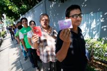 Myanmar national, who gave his name only as Frankie (R), and fellow Burmese San Mint (2-R) show their passport and ID card as they queue outside the Myanmar Embassy waiting for their turn to vote early in Bangkok, Thailand, 17 October 2015. Photo: Diego Azubel/EPA
