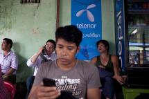 A man uses the internet with a mobile phone in front of Telenor's cheap sim card advertising in Yangon. Photo: Ye Aung Thu/AFP
