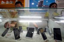 Employees work behind the mobile phone handsets displayed at a mobile phone shop in Yangon, Myanmar, June 28, 2013. Photo: Lynn Bo Bo/EPA
