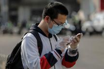 A student wearing a face mask and gloves uses his mobile phone as he leaves a high school in Beijing.
