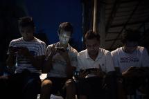 Young men browse their Facebook wall on their smartphones as they sit in a street in Yangon. Photo: Nicolas Asfouri/AFP
