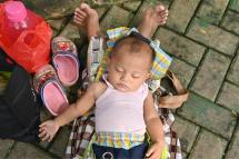 A baby sleeps on his mother’s legs as children play at a play ground in Jakarta on March 29, 2022. Photo: AFP