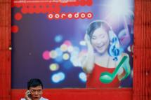 A man speaks on his mobile phone in front of a building with Ooredoo telecom advertising at downtown area in Yangon. Photo: Lynn Bo Bo/EPA