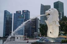A woman is dwarfed by the Merlion statue and buildings of the financial district in Singapore. Photo: EPA