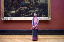 (File) Myanmar pro-democracy leader Aung San Suu Kyi poses in front of the painting "La Liberte guidant le peuple" (Liberty Guiding the People) by French artist Eugene Delacroix, during a visit at the Louvre Museum in Paris on June 29, 2012. Photo: AFP
