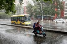 People ride an electric scooter during a downpour in Beijing, China, 30 July 2023. Photo: EPA