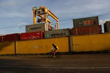 A man drives a bicycle as he passes near containers piled up at a cargo port near Yangon river, Yangon, Myanmar, 09 August 2020. Photo: Lynn Bo Bo/EPA