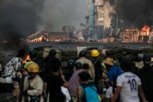 Police officers (background) take position along a road as protesters take cover behind makeshift barricades during a crackdown on demonstrations by protesters against the military coup in Yangon on March 16, 2021. Photo: AFP