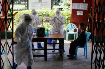 A woman (R) sits near medical workers wearing PPE (Personal protective equipment) to undergoes a swab test for coronavirus disease (COVID-19) at a community quarantine center in Yangon, Myanmar, 27 September 2020. Photo: Lynn Bo Bo/EPA
